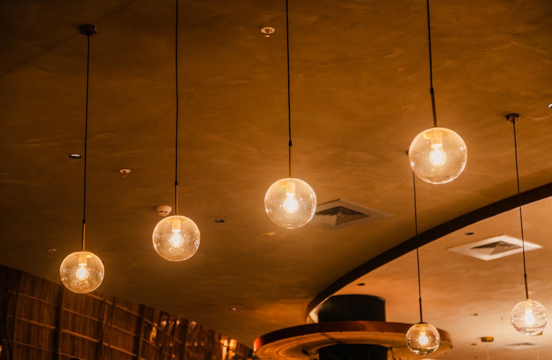 The image displays several pendant lights hanging from the ceiling, each featuring a single light bulb encased in a clear, spherical glass globe. The lights emit a warm glow, creating an inviting and cozy ambiance. The ceiling is finished with a textured surface, adding to the modern and elegant interior design. The arrangement of the lights and their soft illumination enhance the overall aesthetic of the space.